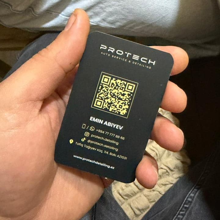 Əldə tutulan çap olunmuş PROTECH vizit kartı: tünd boz fonda loqo, qızılı QR kod, ad, telefon və WhatsApp nömrəsi, sosial şəbəkə ünvanları, ünvan və veb-sayt.
